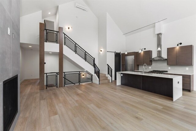 kitchen featuring wall chimney exhaust hood, an island with sink, and high vaulted ceiling