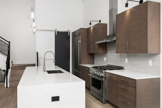 kitchen with sink, wall chimney exhaust hood, premium appliances, a barn door, and an island with sink