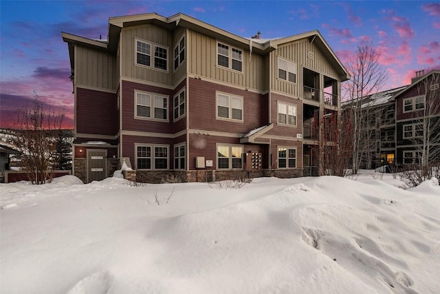 snow covered house featuring board and batten siding and stone siding