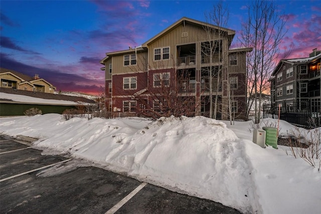 snow covered back of property featuring uncovered parking, a balcony, and board and batten siding