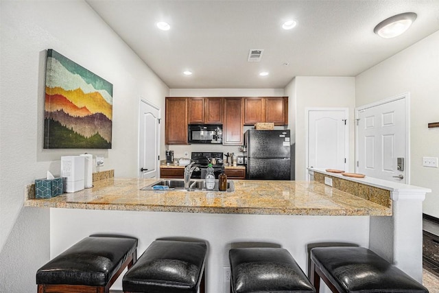 kitchen with a kitchen breakfast bar, visible vents, tile countertops, a sink, and black appliances