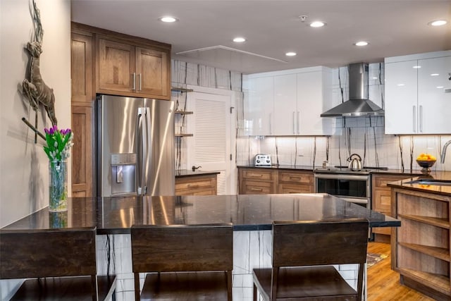 1875 Ski Time Square Dr Unit 711, Steamboat Springs, CO 80487 - kitchen with a kitchen breakfast bar, a sink, light wood-type flooring, wall chimney range hood, and appliances with stainless steel finishes