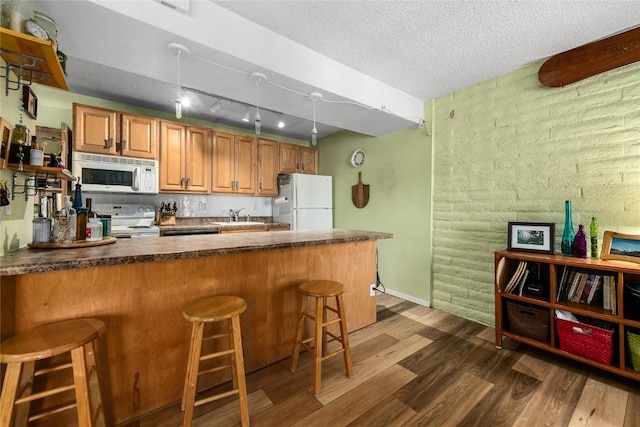 21 Balsam Ct, Steamboat Springs, CO 80487 - kitchen featuring a peninsula, dark wood finished floors, a kitchen bar, white appliances, and brown cabinets