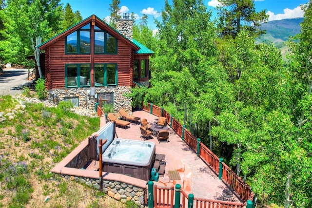 back of house featuring stone siding, a chimney, log exterior, a patio area, and a hot tub