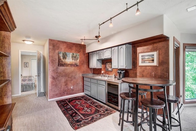 kitchen featuring beverage cooler, baseboards, light carpet, and gray cabinetry
