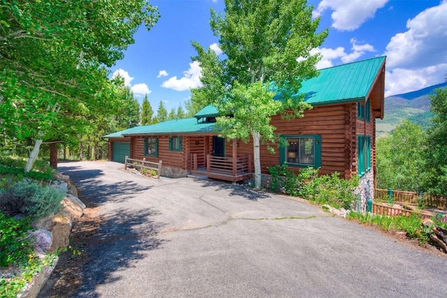 log-style house with aphalt driveway, a garage, log siding, a porch, and metal roof