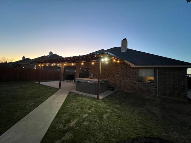 back of property with a patio area, a lawn, a chimney, fence, and a hot tub
