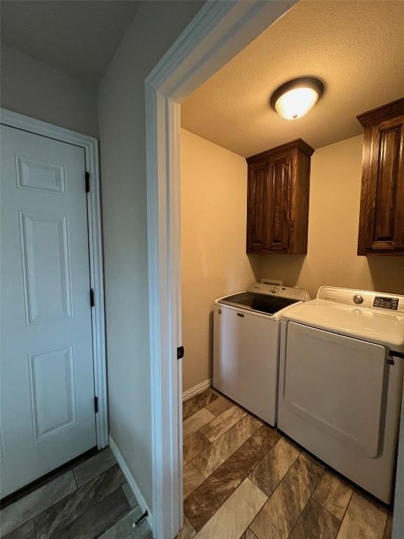 clothes washing area featuring cabinet space, stone finish floor, washing machine and clothes dryer, and baseboards