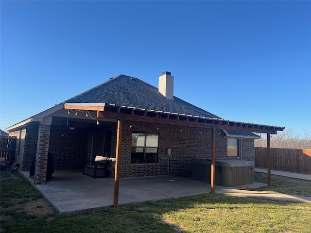 back of property with a chimney, fence, brick siding, a patio area, and a hot tub