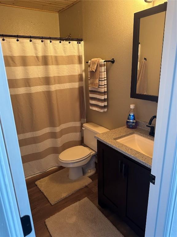 full bathroom with a textured wall, wood finished floors, vanity, and toilet