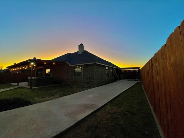 view of side of property featuring a patio area, a hot tub, a fenced backyard, and a chimney