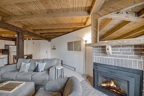 8500 Ryan Gulch Rd Unit 101, Silverthorne, CO 80498 - living room with wooden ceiling, a warm lit fireplace, beamed ceiling, a baseboard radiator, and brick patterned floors