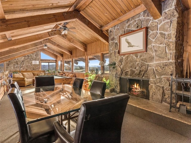 dining area with vaulted ceiling with beams, ceiling fan, a stone fireplace, and wooden ceiling