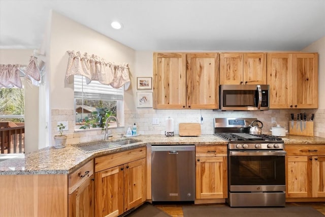 kitchen with a sink, light stone counters, plenty of natural light, and stainless steel appliances