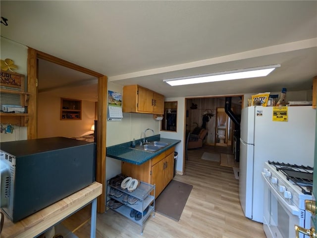 kitchen with brown cabinetry, a sink, dark countertops, light wood-type flooring, and white gas range oven