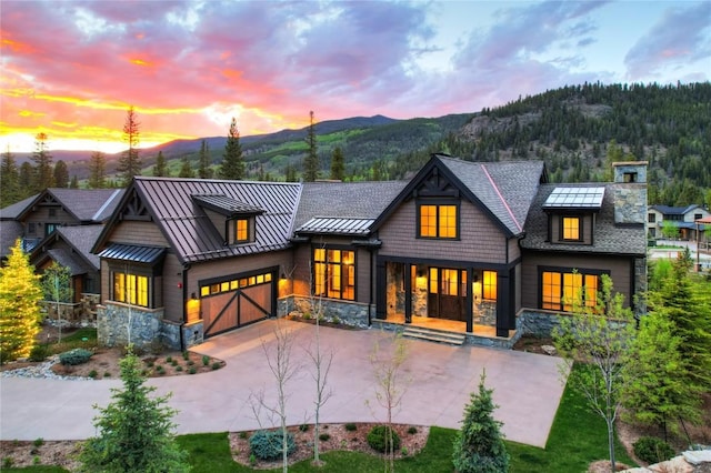 77 E Trade Ct, Keystone, CO 80435 - back of house at dusk with a standing seam roof, a mountain view, driveway, stone siding, and metal roof