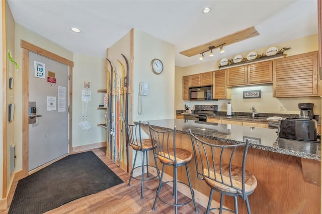 kitchen featuring black microwave, a kitchen breakfast bar, light wood-style floors, and electric range oven