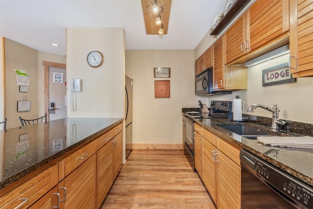 kitchen featuring light wood finished floors, a sink, dark stone counters, brown cabinets, and black appliances