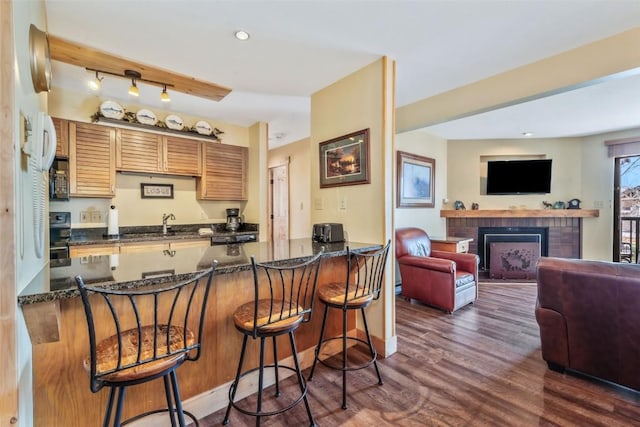 kitchen featuring dark wood-type flooring, a fireplace, dark stone counters, and a breakfast bar area