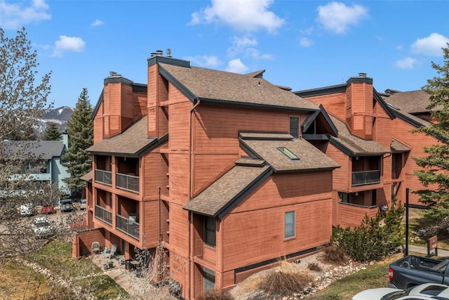 view of side of home with a shingled roof, a chimney, and a balcony