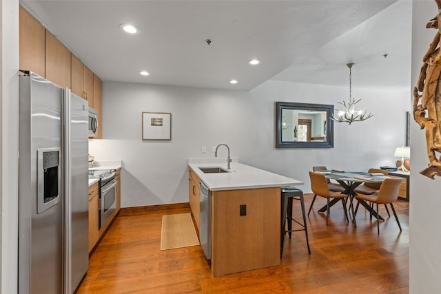 kitchen with kitchen peninsula, appliances with stainless steel finishes, a kitchen bar, sink, and pendant lighting