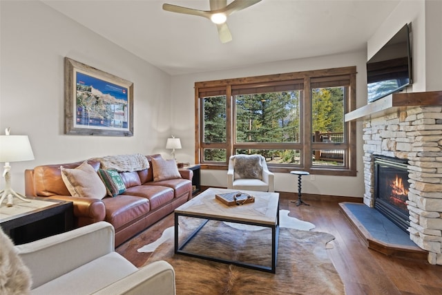 living room featuring dark hardwood / wood-style floors, ceiling fan, and a stone fireplace