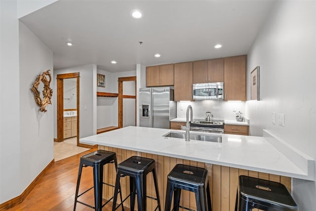 kitchen with sink, light hardwood / wood-style flooring, kitchen peninsula, a kitchen bar, and appliances with stainless steel finishes