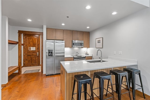 kitchen with kitchen peninsula, appliances with stainless steel finishes, a kitchen bar, light wood-type flooring, and sink