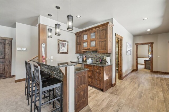 28 Tieze Ln, Keystone, CO 80435 - kitchen featuring a breakfast bar area, dark stone countertops, brown cabinetry, tasteful backsplash, and glass insert cabinets