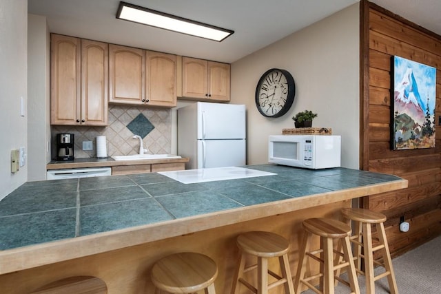 kitchen featuring a sink, a kitchen bar, decorative backsplash, white appliances, and light brown cabinets