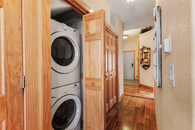 clothes washing area with visible vents, baseboards, wood finished floors, stacked washing maching and dryer, and laundry area