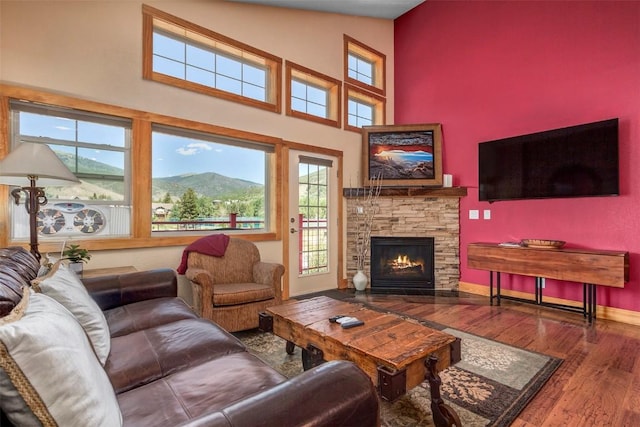 living area with a high ceiling, a healthy amount of sunlight, wood finished floors, and a fireplace