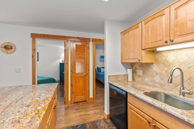 kitchen with wood finished floors, a sink, backsplash, light stone countertops, and black dishwasher