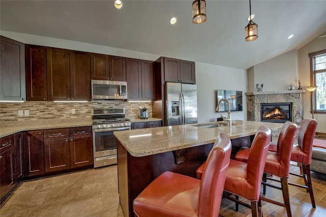 kitchen featuring appliances with stainless steel finishes, a kitchen breakfast bar, hanging light fixtures, lofted ceiling, and an island with sink