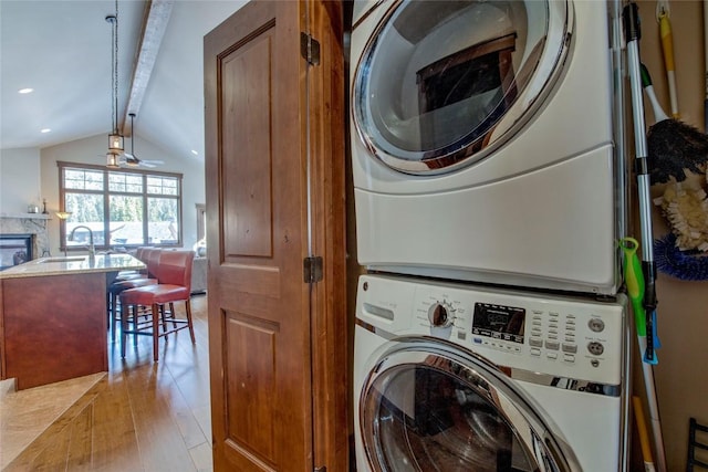 clothes washing area with light wood-type flooring, ceiling fan, stacked washer and clothes dryer, and sink