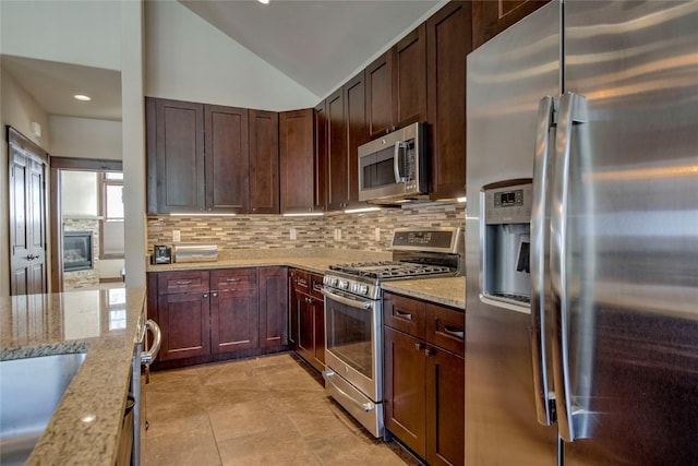 kitchen featuring lofted ceiling, backsplash, sink, light stone countertops, and appliances with stainless steel finishes