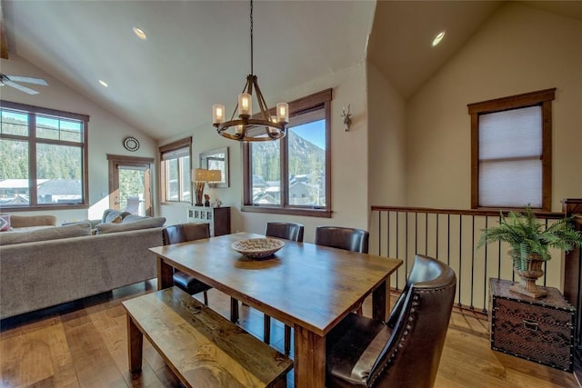 dining area with ceiling fan with notable chandelier, light wood-type flooring, and vaulted ceiling