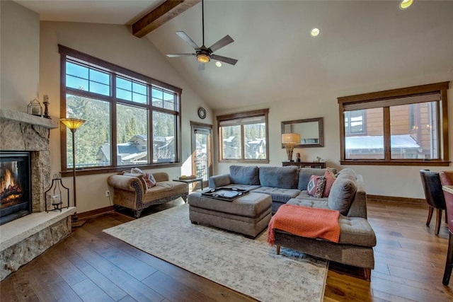 living room featuring beam ceiling, a stone fireplace, ceiling fan, and dark wood-type flooring