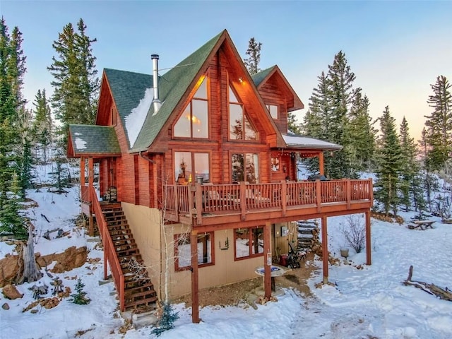 snow covered house with a deck, stairway, and roof with shingles