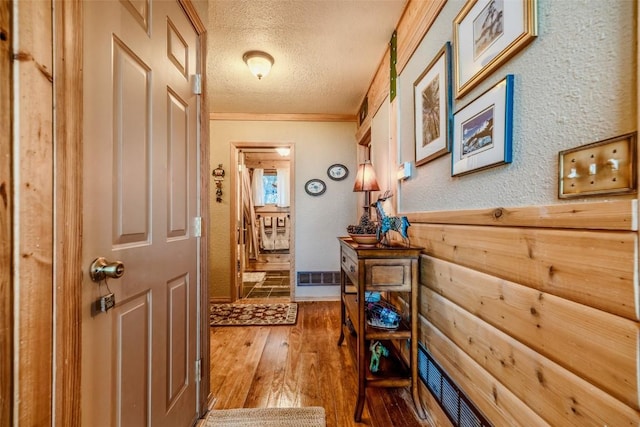 hall with a textured ceiling, wood-type flooring, crown molding, and a textured wall