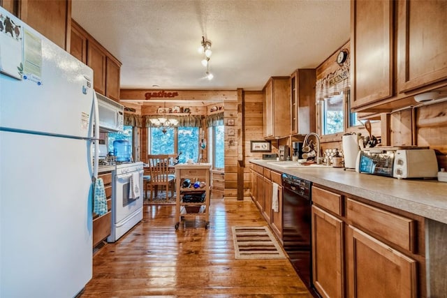 kitchen featuring white appliances, a sink, brown cabinets, a textured ceiling, and wooden walls