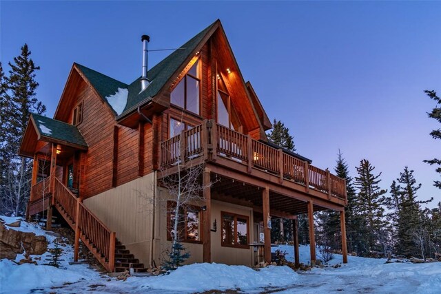 snow covered back of property with a wooden deck and stairway