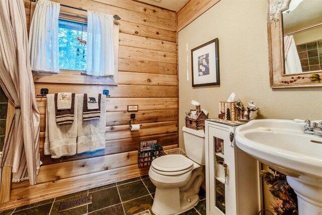 full bath with toilet, wood walls, tile patterned flooring, and a sink