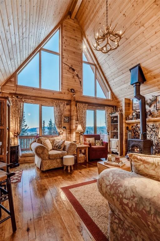 bedroom featuring high vaulted ceiling, a chandelier, a wood stove, wood ceiling, and hardwood / wood-style floors