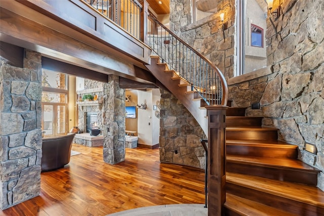 staircase with wood-type flooring, a high ceiling, and a fireplace