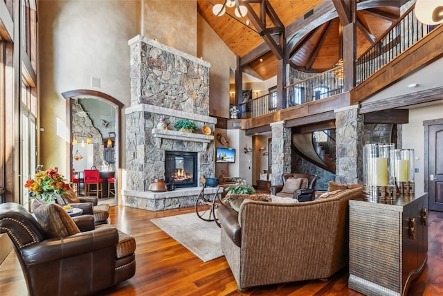 living area with wooden ceiling, beamed ceiling, hardwood / wood-style flooring, a stone fireplace, and high vaulted ceiling