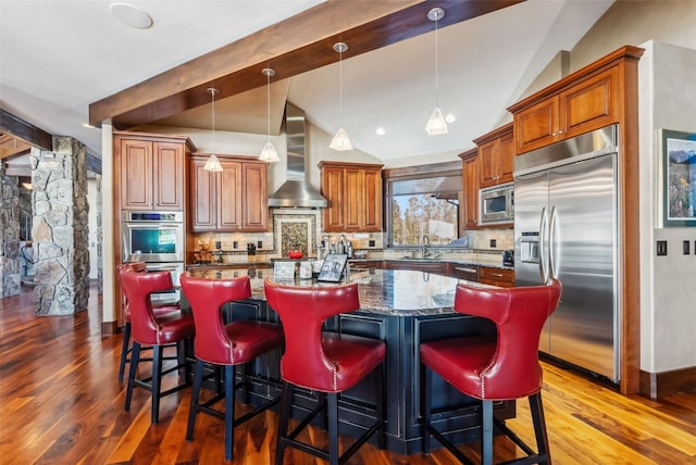 kitchen featuring wall chimney exhaust hood, built in appliances, lofted ceiling with beams, and tasteful backsplash