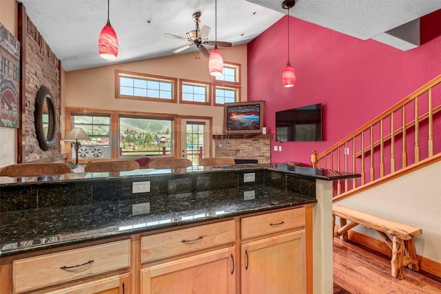 kitchen with ceiling fan, light hardwood / wood-style floors, pendant lighting, vaulted ceiling, and dark stone countertops