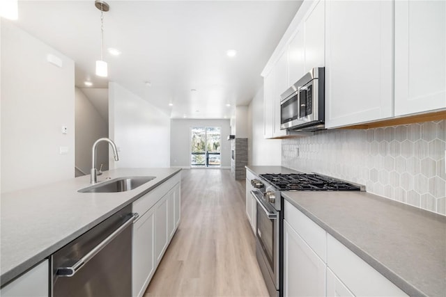 kitchen with white cabinets, stainless steel appliances, a sink, light wood-style floors, and hanging light fixtures