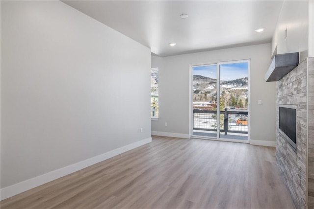 unfurnished living room featuring baseboards, wood finished floors, a large fireplace, and recessed lighting